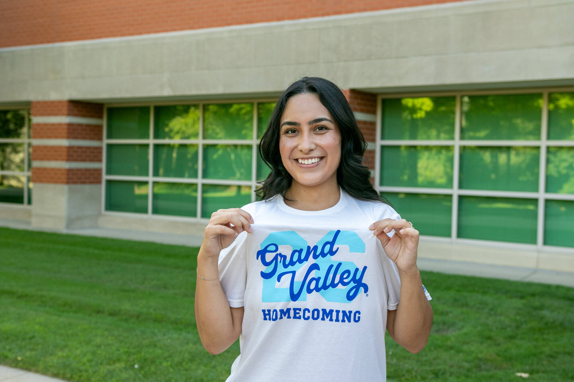 A student smiles wearing the GVSU Homecoming T-shirt on campus